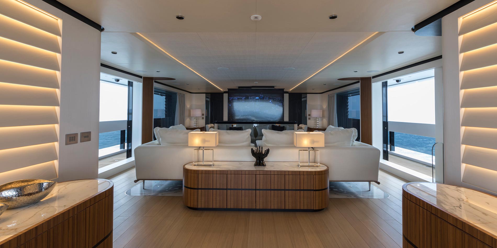 Luxury yacht interior with warm architectural lighting, white sofas, and custom wood finishes